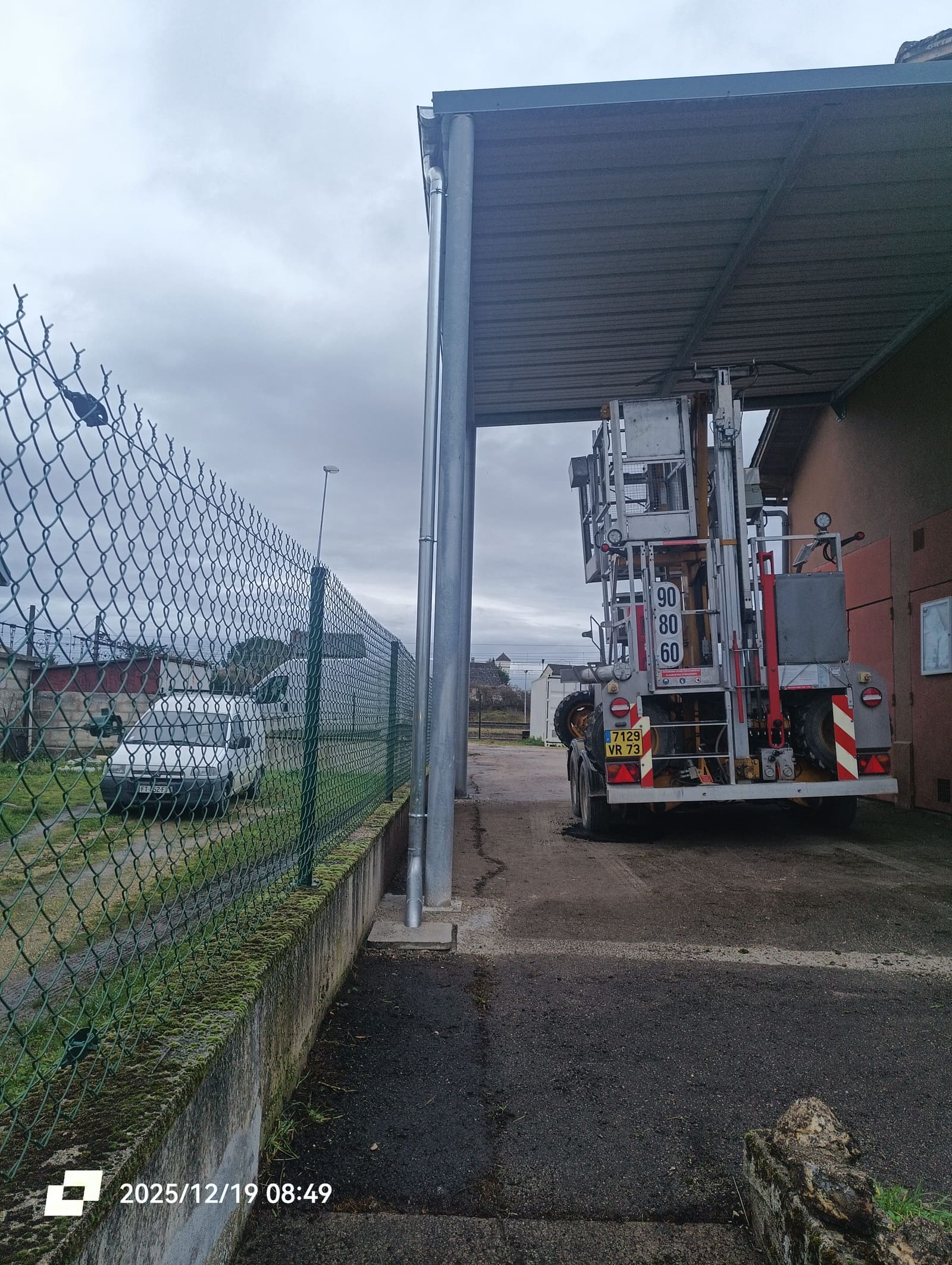Abri à engins couvert en bac acier sur poteaux métalliques, abritant un camion nacelle ferroviaire