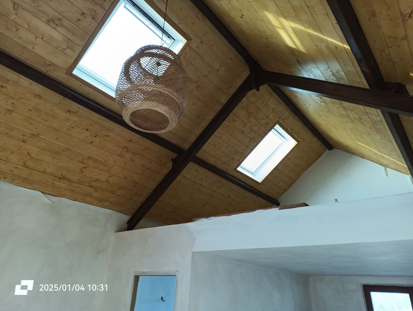 Combles aménagés terminés : plafond en lambris clair, poutres apparentes foncées et deux fenêtres de toit