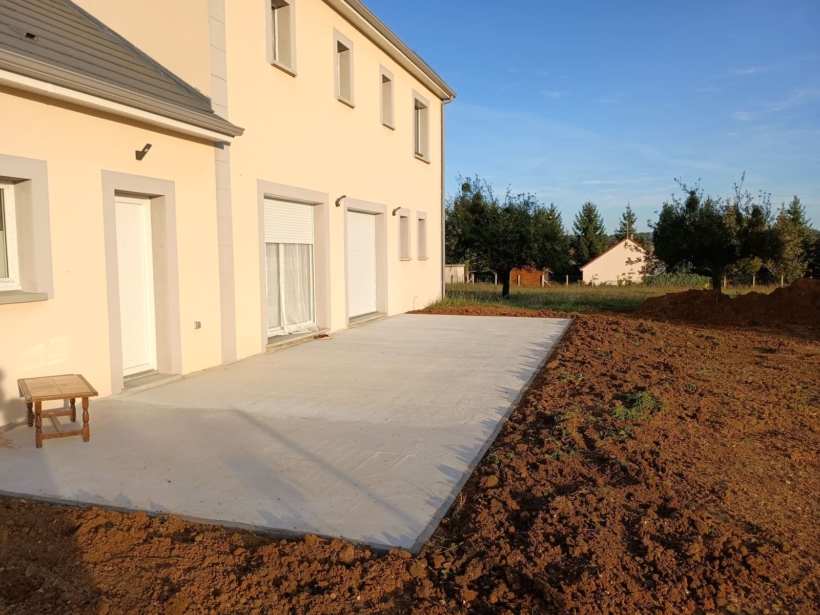 Dalle béton fraîchement coulée et talochée devant une maison neuve, terrain encore en terre