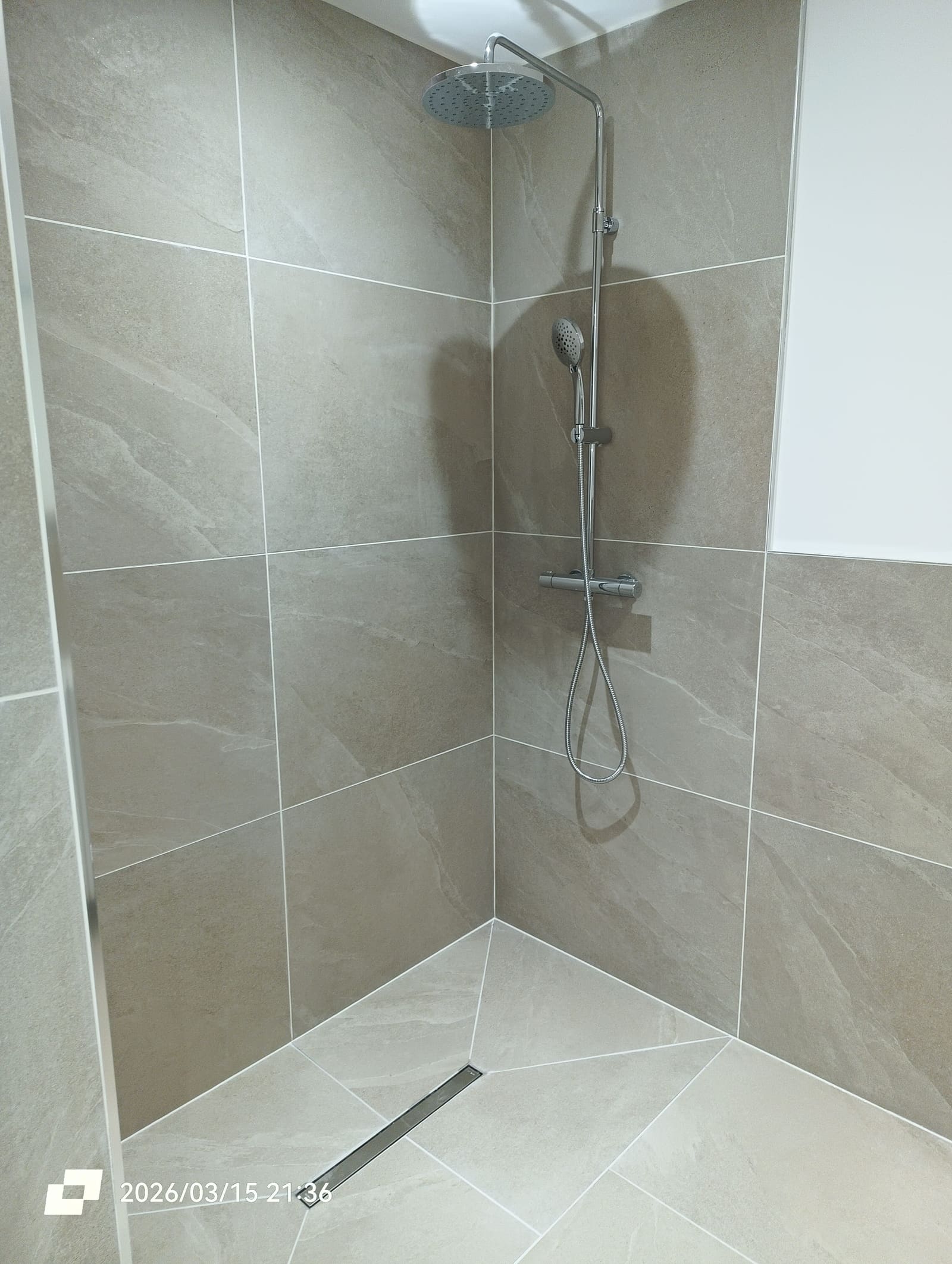 Douche à l’italienne carrelée en grand format avec caniveau linéaire et colonne de douche encastrée