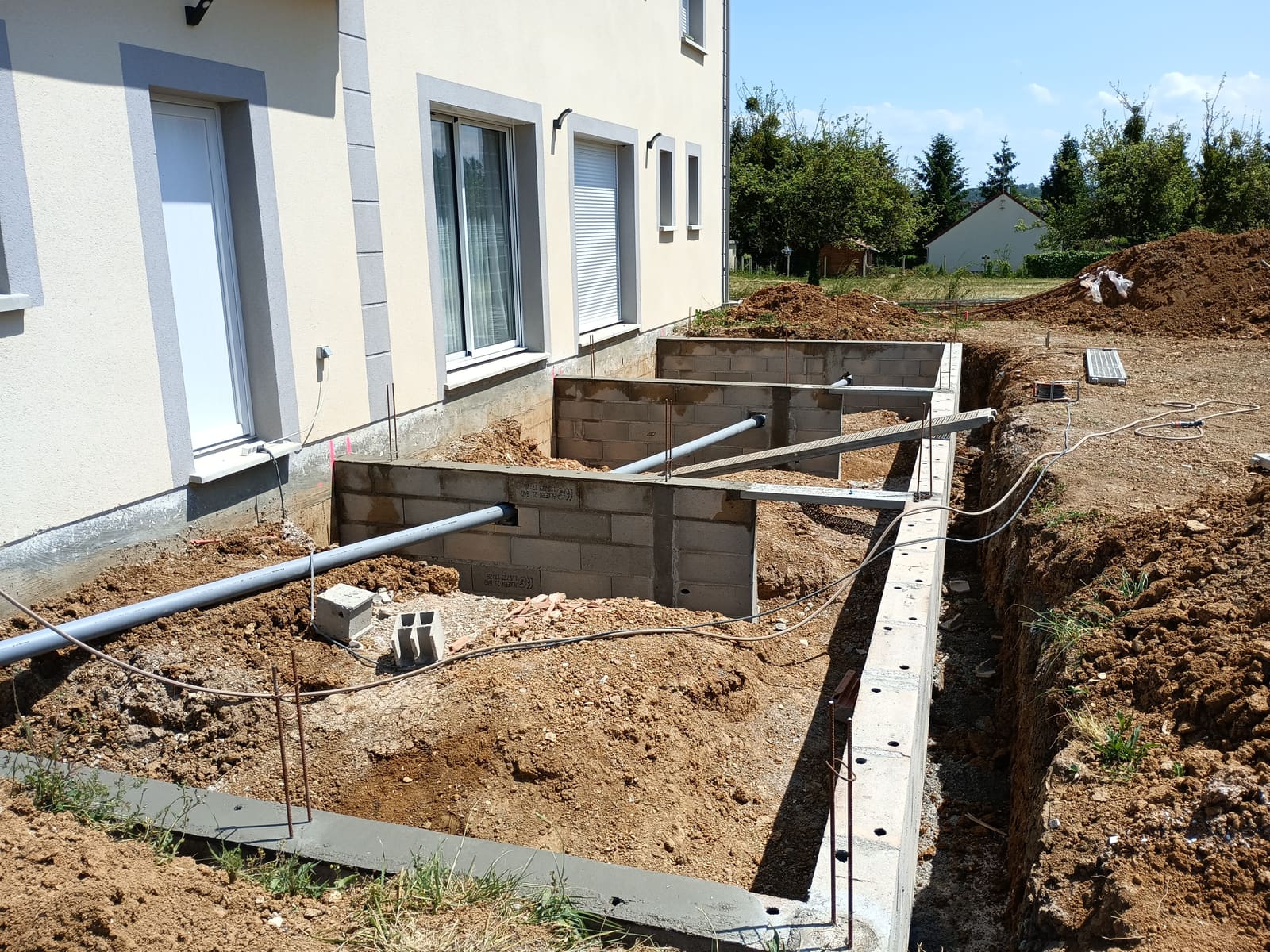 Semelle filante et premiers rangs de blocs béton coulés le long d’une maison, en préparation d’une extension