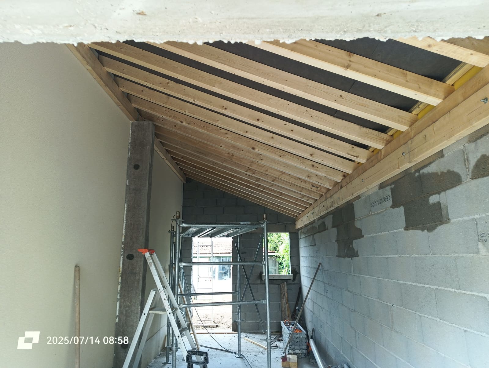 Charpente bois neuve vue de l’intérieur du garage, chevrons et écran sous-toiture posés sur les murs en blocs béton