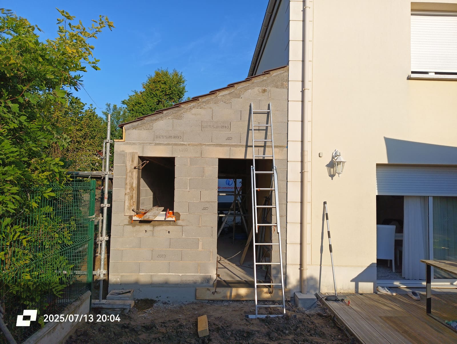 Élévation d’un garage en blocs béton accolé à une maison, échafaudage en place et ouverture de porte réservée