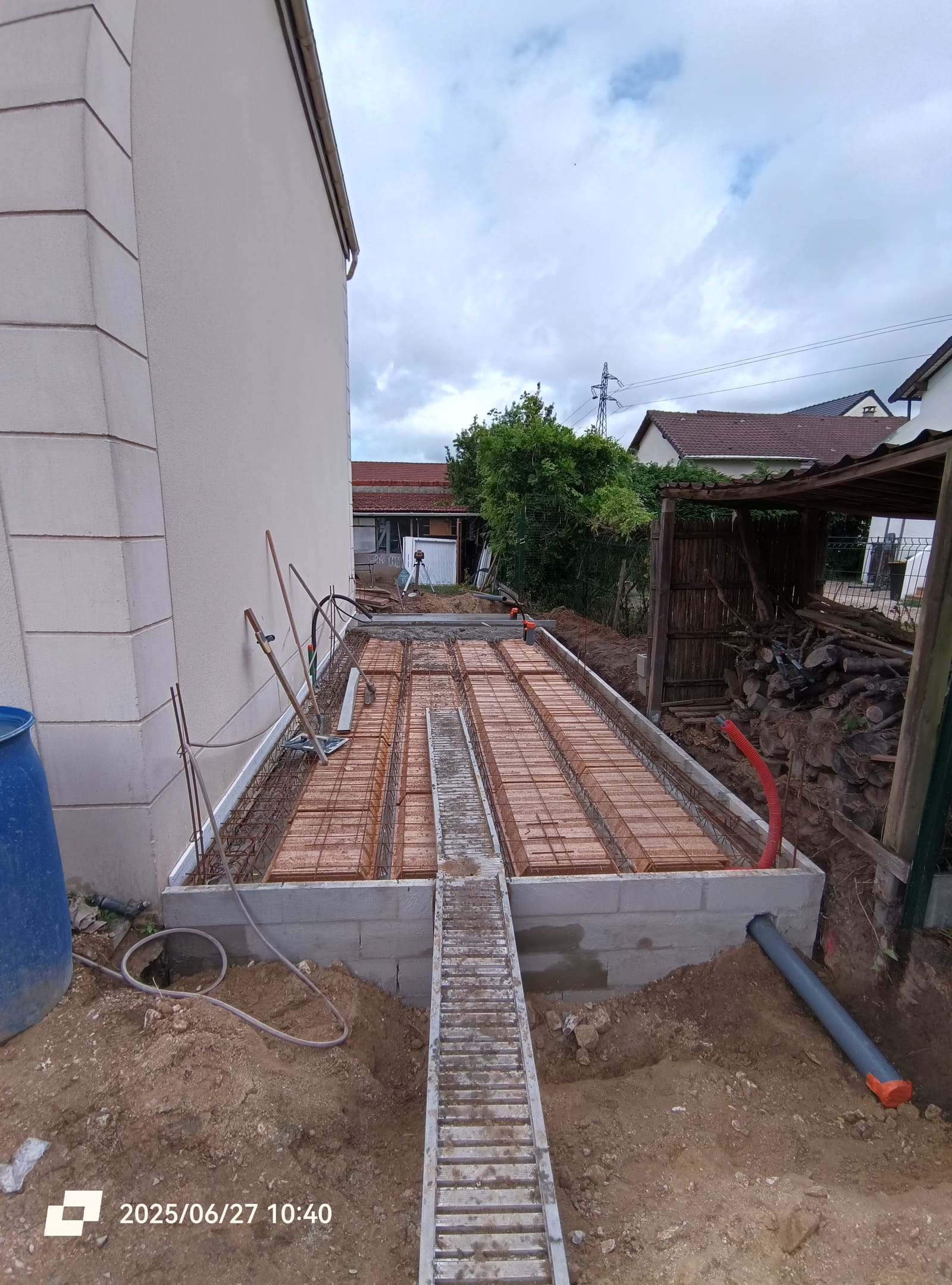 Fondations de garage coulées avec ferraillage en attente et réseaux enterrés, contre le pignon d’une maison