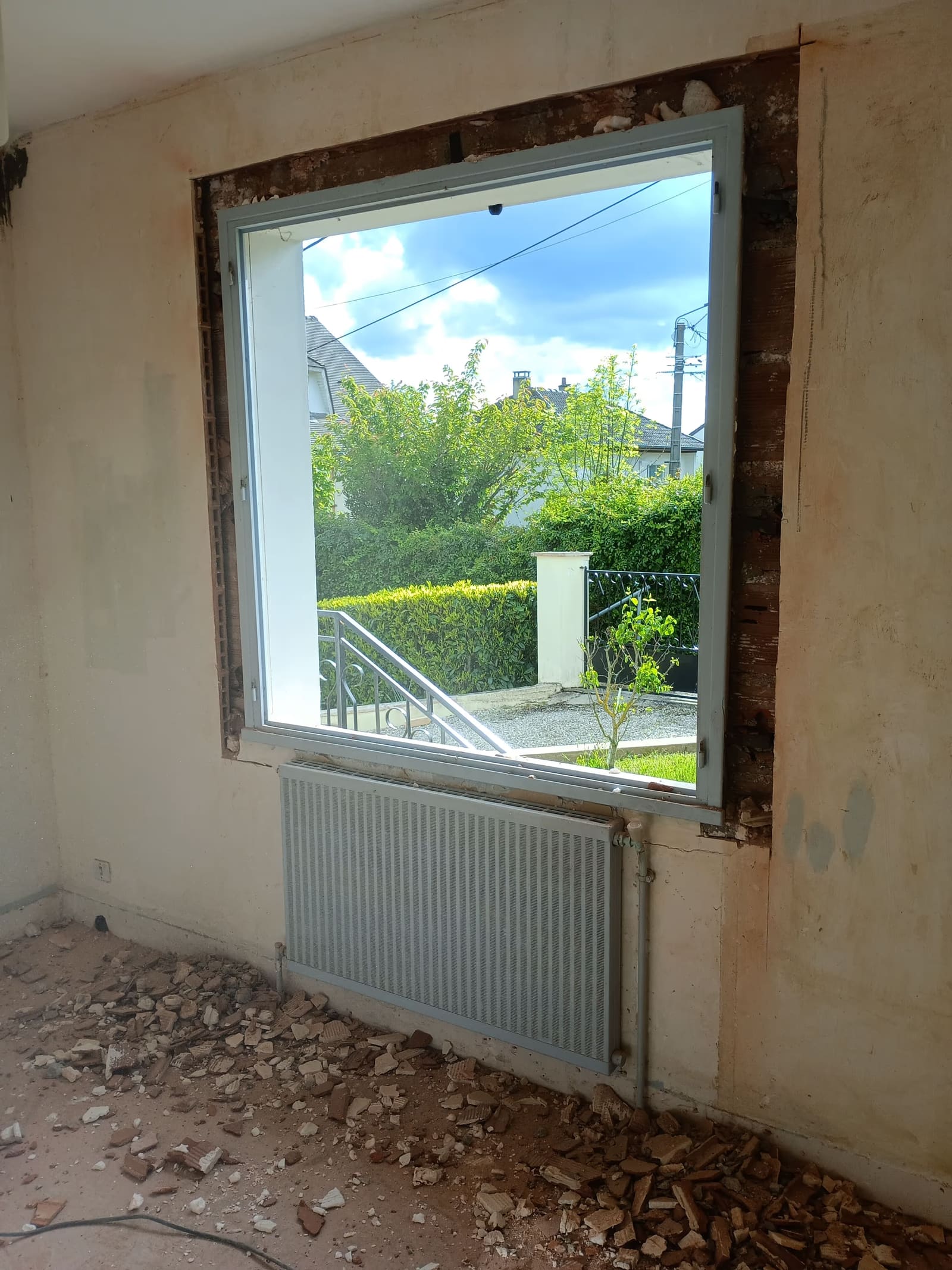 Baie vitrée neuve posée dans un mur en pierre décroûté, pendant la rénovation d’une pièce de vie