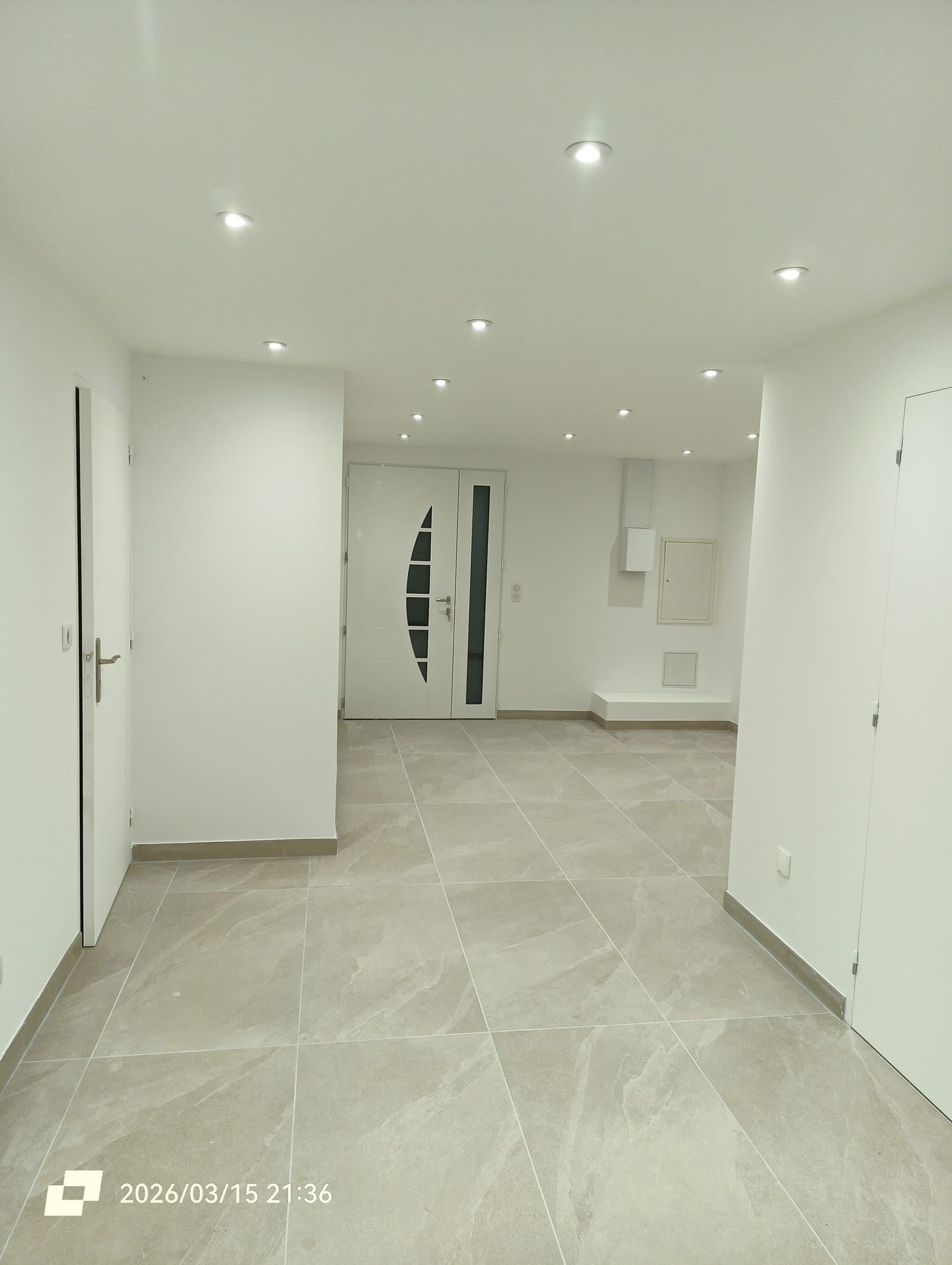 Entrée rénovée avec porte vitrée, plafond à spots encastrés et carrelage grand format posé en continu