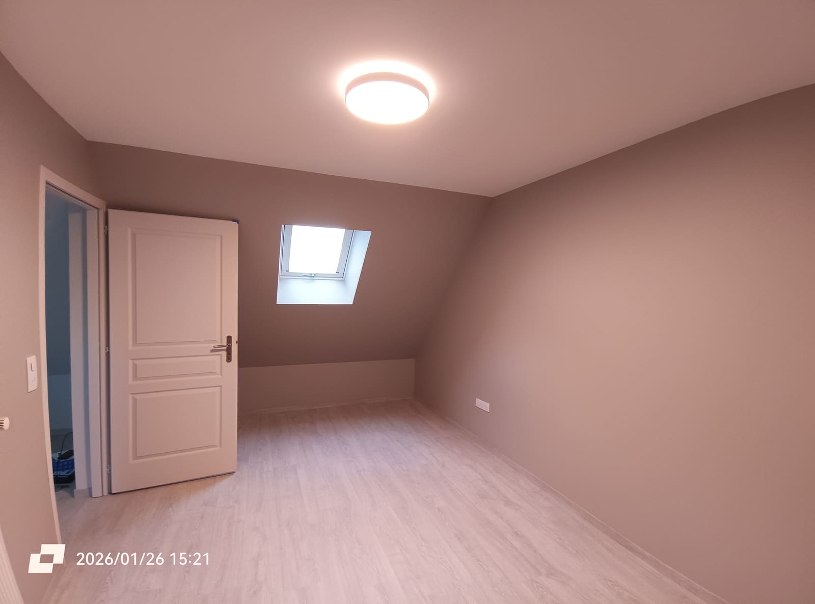 Chambre sous rampants terminée : murs vieux rose, sol stratifié clair et fenêtre de toit