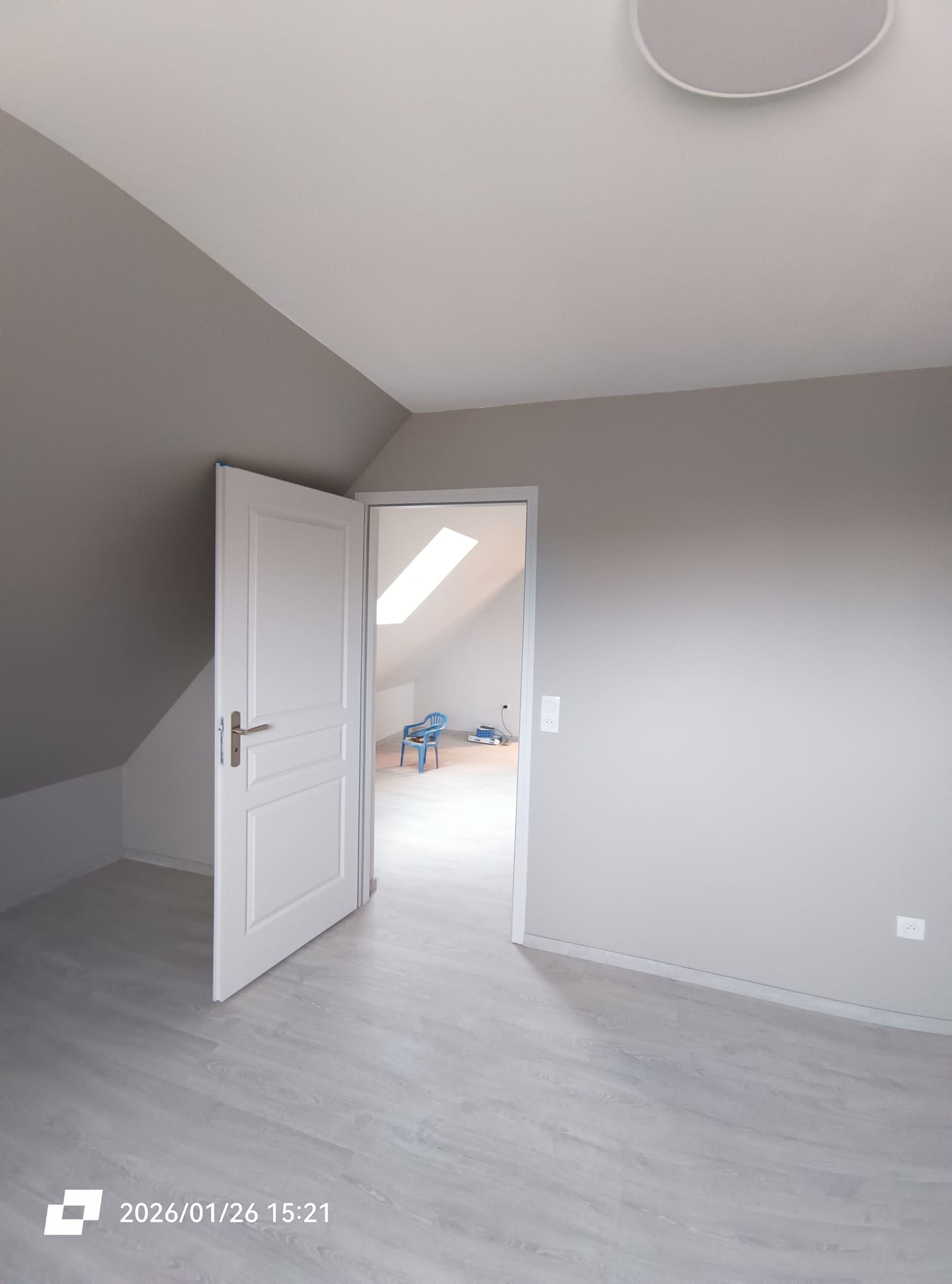 Chambre terminée aux murs taupe, porte ouverte sur une seconde chambre sous rampants