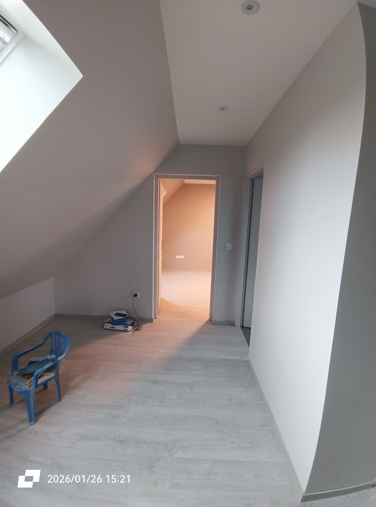 Palier de l’étage terminé sous rampants, sol stratifié clair et ouverture sur une chambre