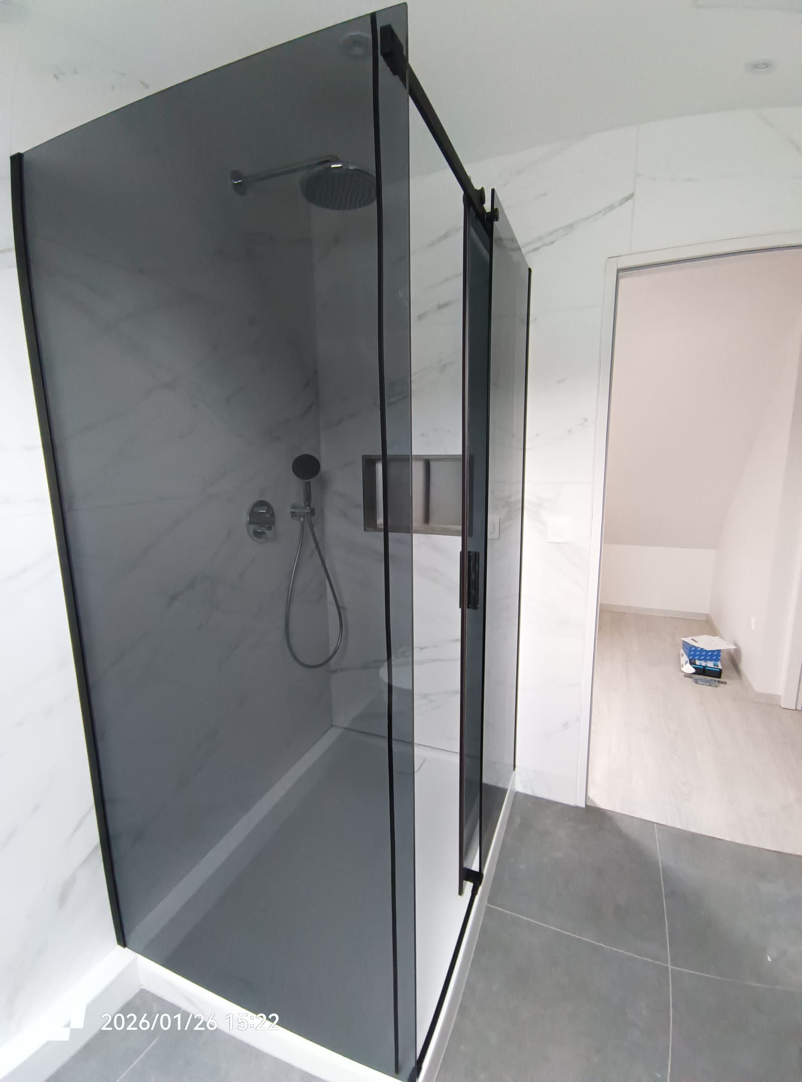 Douche à l’italienne avec paroi en verre fumé sur profilés noirs et faïence effet marbre blanc