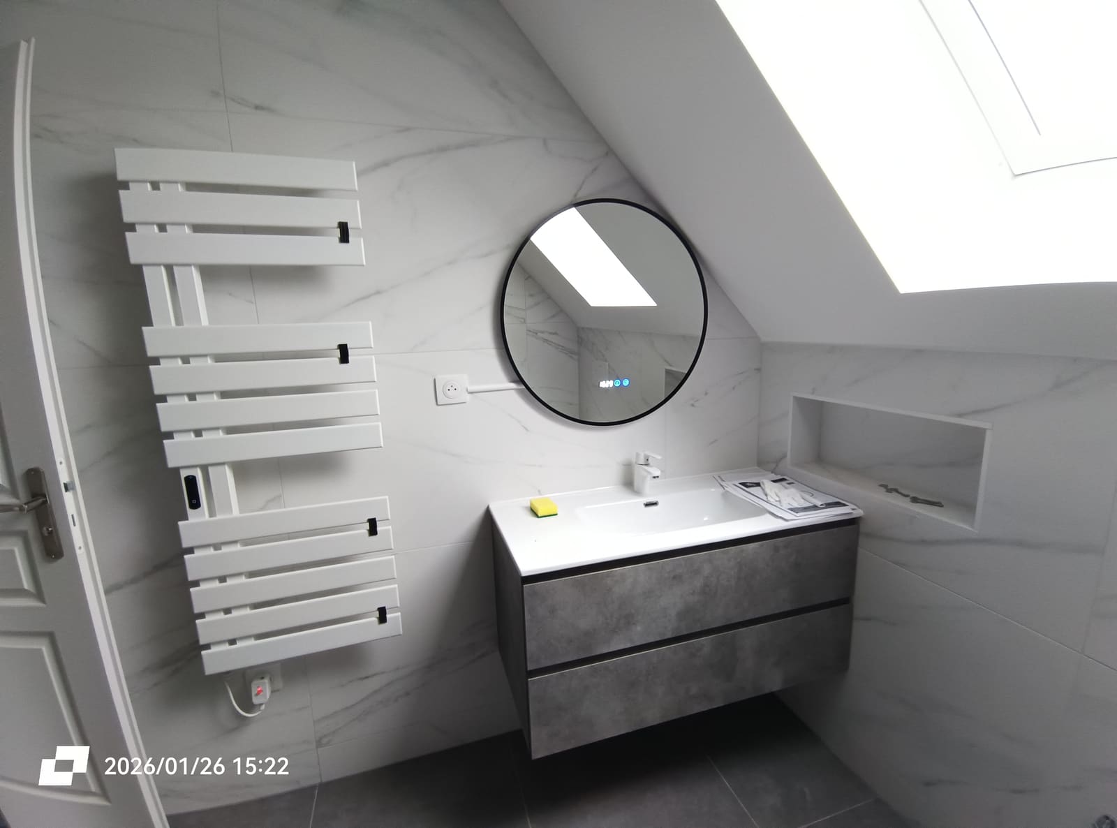 Meuble vasque suspendu effet béton, miroir rond rétroéclairé et sèche-serviettes, sous rampant avec fenêtre de toit