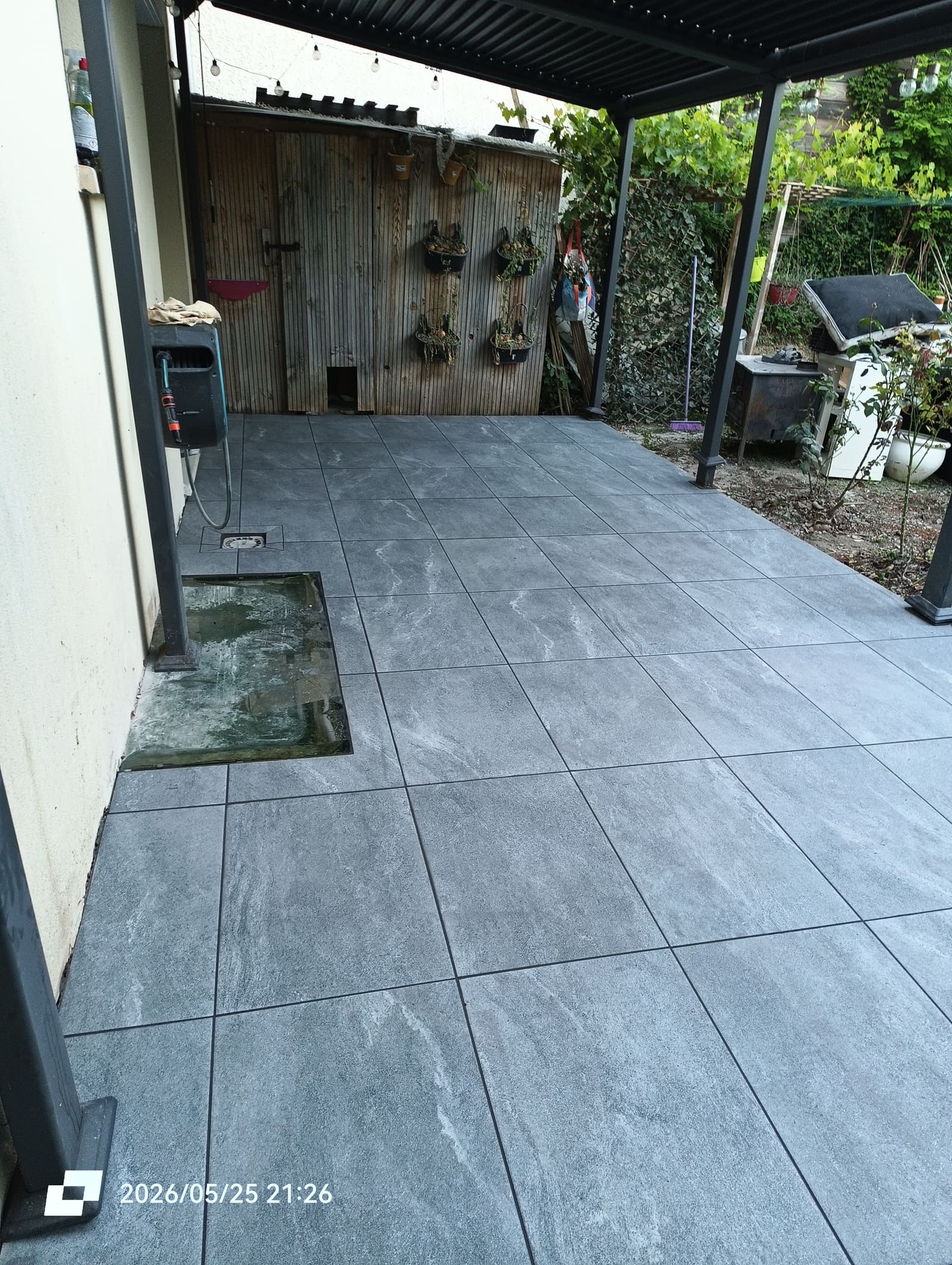 Terrasse carrelée en grès cérame gris anthracite sous une pergola à structure métallique noire